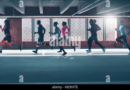 Gruppo di diversi giovani running urbano di fronte la luminosa griglie sulle finestre di un parcheggio al coperto e sacco Foto Stock