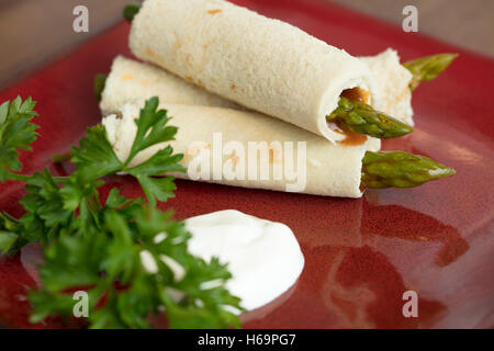 Gli asparagi arrotolato nel pane appiattita con una medicazione russo e panna acida guarnite con prezzemolo Foto Stock