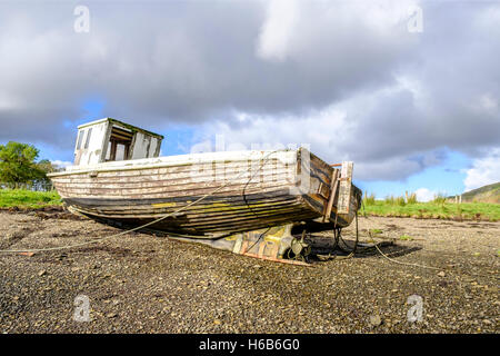 Sole risplende sulla vernice di pelatura del esposta la parte inferiore di un abbandonato la barca di legno naufragio sulle rive di Loch Harport sull isola Foto Stock