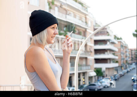 Young Teen donna il fumo di sigarette e sorridente outdoor con la scena urbana in background Foto Stock