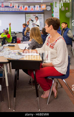 Un osservatore professionale prende appunti mentre è seduto in una scuola elementare in classe Mission Viejo, CA. Nota che gli studenti e il maestro ignorare l'osservatore come andare circa le loro attività. Foto Stock