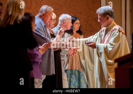 A San Timoteo della Chiesa Cattolica, Laguna Niguel, CA, a monsignor distribuisce ostie a Echaristic ministri che assiste il sacerdote nell amministrare i sacramenti della santa comunione, del pane e del vino consacrati Foto Stock