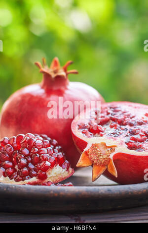 Mature melograno frutto servito sulla piastra rustico in natura. Verde sfondo sfocato con abbondanza di spazio di copia Foto Stock