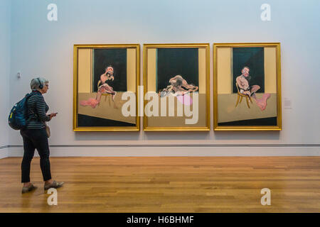 Un vecchio femmina con il suo tour audio telefoni di testa si erge davanti a Francis Bacon trittico in un museo mostra il suo lavoro. Foto Stock