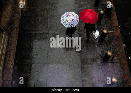 Un paio di ombrelli azienda cammina su un marciapiede di Manhattan dalla Grand Central Station su una piovosa mattinata. Foto Stock
