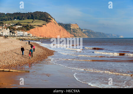 Visitatori godendo di fine ottobre sole sulla spiaggia a Sidmouth, nel Devon, Regno Unito. Città, Esplanade e la Jurassic Coast scogliere in background Foto Stock