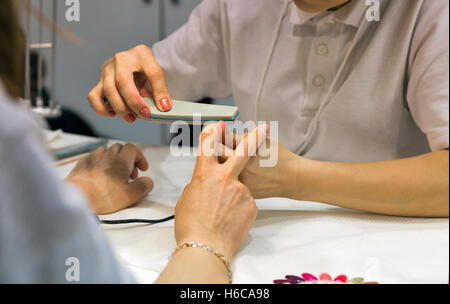 Manicurist master chiodo rende il deposito sulla donna mano closeup, il fuoco selettivo Foto Stock