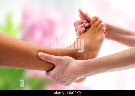 Extreme close up del terapista facendo massaggio osteopatico sul piede femminile. Sfondo colorato. Foto Stock