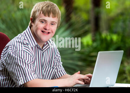 Ritratto di felice handicappati giovane digitando su laptop in giardino. Foto Stock