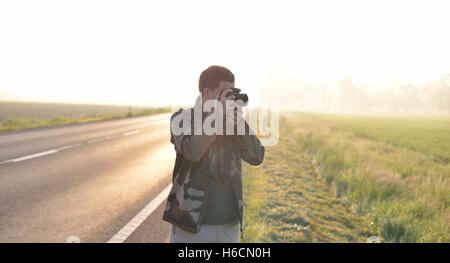 Paesaggio fotografo professionista di scattare una foto vicino a una strada con il sorgere del sole in background Foto Stock