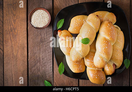 Salsicce in pasta cosparsi di semi di sesamo su un sfondo di legno in stile rustico Foto Stock