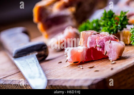 Materie fette di pancetta affumicata su tavola di legno con cumino e erbe aromatiche. Foto Stock