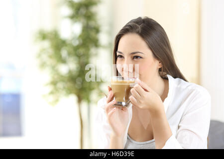 Donna sorseggiando e bere un delizioso caffè con il latte che guarda lontano da casa Foto Stock