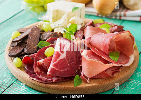 Antipasto piatto di catering con pancetta, a scatti, salsiccia, formaggio blu e Uva su uno sfondo di legno. Foto Stock