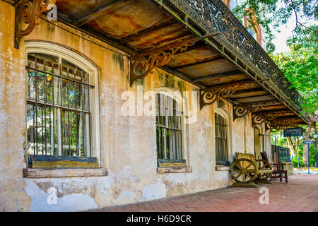 Mattone marciapiede lungo affascinante edificio storico con banco di antiquariato & ornamentali in ferro battuto balcone nel centro di Savannah, GA Foto Stock