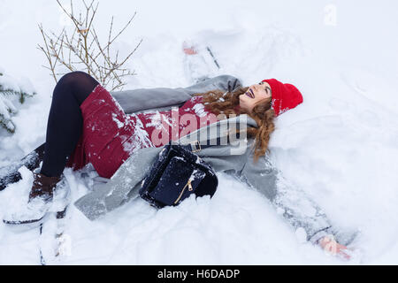 Ritratto di carino affascinante ragazza hipster winter park. Ella fa un angelo di neve. Divertimento invernale. Passeggiate all'aria aperta. Foto Stock