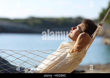 Vista laterale di un casual uomo felice relax su una amaca in spiaggia in vacanza Foto Stock