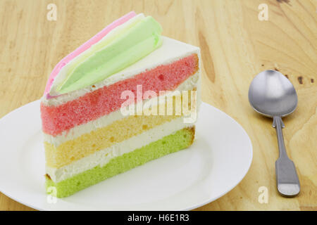 Layer Cake su una piastra bianca con un piccolo cucchiaio posto sul tavolo di legno Foto Stock