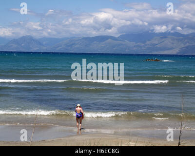 Riluttante lady bagnante presso San Spiridione Beach, Corfu Grecia guardando verso le montagne di Albania Foto Stock