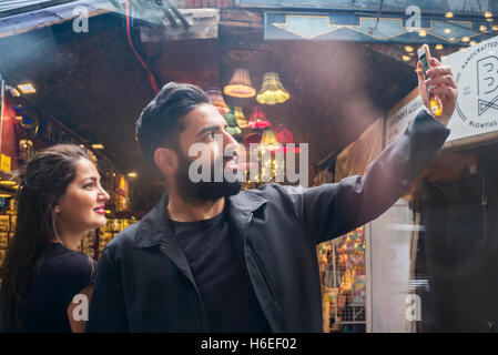 Barbuto dai capelli scuri che l'uomo assume un telefono cellulare selfie di se stesso e la signora in Camden Market Londra Foto Stock