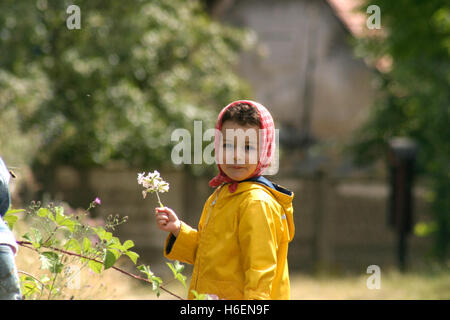 Ritratto di bambina con fazzoletto rosso al di fuori su di un campo con fiore in mano Foto Stock