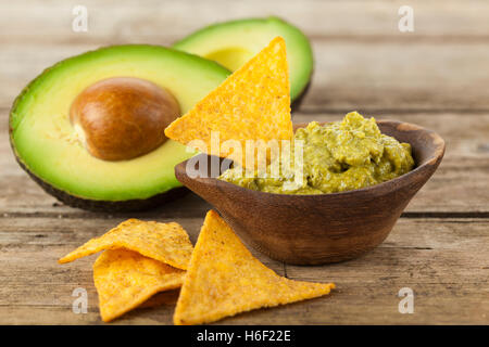 Ciotola di legno riempita con salsa guacamole, nachos e dimezzato avocado sul tavolo rustico Foto Stock