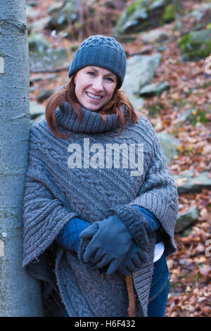 Una donna glamour escursioni attraverso i boschi in autunno caduta stagione indossando un informale poncho di lana di abbigliamento per il tempo libero cappellino guanti Foto Stock