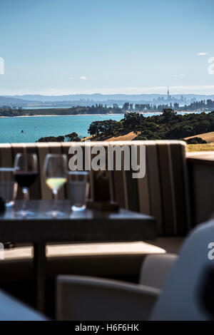 Una cantina sull isola di Waiheke con vino rosso e bianco sul tavolo alla zona salotto ombreggiata. Auckland, Nuova Zelanda lo skyline della citta'. Foto Stock