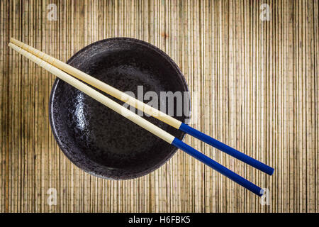 Bacchette e Riso o Noodle bowl contro un tappetino di bambù lo sfondo ideale per piatti Asiatici soggetti Foto Stock