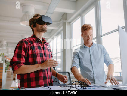 Giovane sviluppatore che lavora sul computer portatile e occhiali per realtà virtuale. Due uomini migliorando la realtà virtuale bicchieri in ufficio. Foto Stock