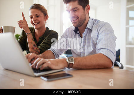 Colpo di coppia giovane alla tabella utilizzando il portatile a casa. Allegro giovane uomo e donna che lavorano su laptop. Foto Stock