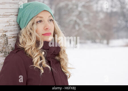 Donna appoggiata ad albero in inverno Foto Stock
