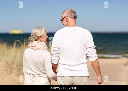 Felice coppia senior tenendo le mani sulla spiaggia di estate Foto Stock