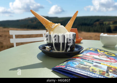 Immagine composita di indesiderate devon clotted coni gelato immersi in cappuccino su un verde giardino esterno tabella in dartmoor sunshine. Foto Stock