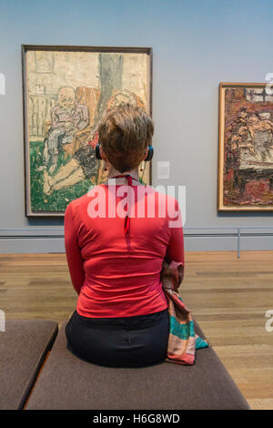 Una donna si siede di fronte a un dipinto in un museo di arte ascoltando l'audio tour dell'opera d'arte sulle cuffie. Foto Stock