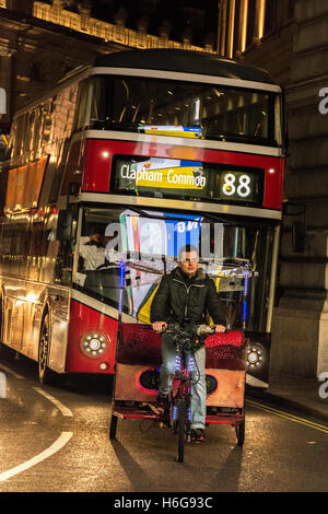 Un risciò e un autista e gli autobus notturni passano attraverso un Piccadilly Circus illuminato e luminoso nel centro di Londra, Regno Unito Foto Stock