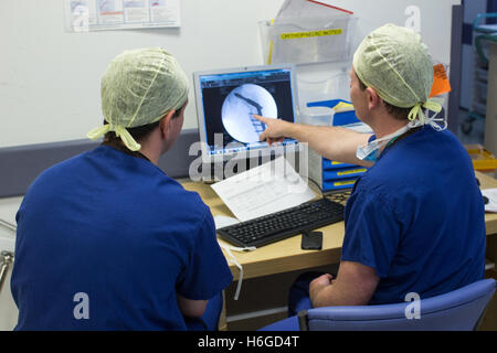 Due medici a discutere di un paziente X Ray sullo schermo che mostra una gamba rotta.Essi discutono le immagini e le note sul telefono cellulare. Foto Stock