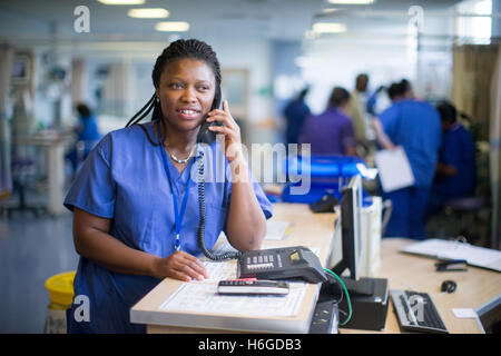 Infermiere ospedale in corrispondenza di una stazione di lavoro in un reparto a rispondere alle richieste di informazioni e controllare i record medici Foto Stock