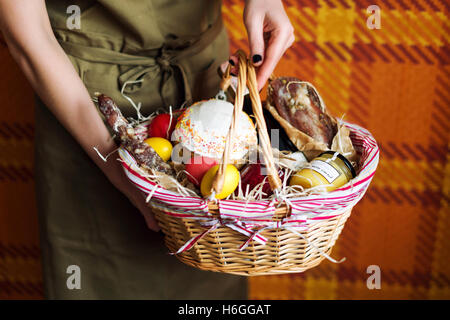 Mani femminili cestello di contenimento con uova colorate, torta, vino rosso, hamon o a scatti e asciutto salsiccia affumicata. Cibo set regalo per celebrare la Pasqua. Foto Stock