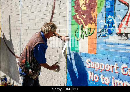 Artista Danny Devenney prepara una parete per un nuovo murale sulla pace internazionale a parete, Falls Road, Belfast. Foto Stock