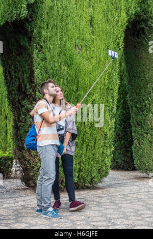 Un giovane adulto sposato Caucasian giovane tenendo selfie foto utilizzando un selfie-stick presso i giardini dell'Alhambra di Granada, Spagna. Foto Stock