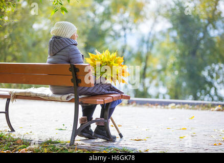 Senior donna seduta sulla panchina nel parco e azienda mazzetto di foglie di autunno Foto Stock