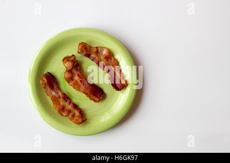 Tre pezzi di pancetta fritta posti in fila su di una piastra verde isolato su uno sfondo bianco Foto Stock