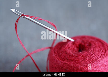 Concetto di cucitura. Extreme closeup di ago in acciaio con filo rosso Foto Stock