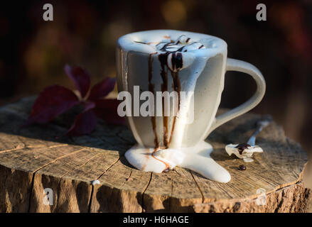 Molto disordinato di cioccolata calda con panna montata e salsa al cioccolato traboccante di una tazza alta impostata sul ceppo di albero Foto Stock