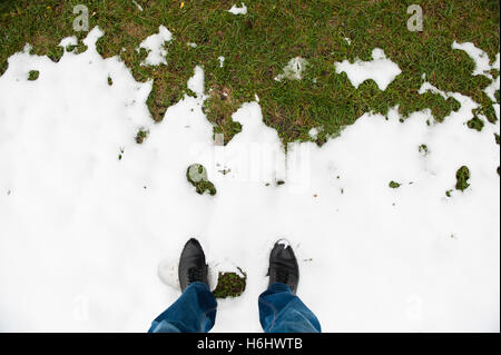 Piedi in mens stivali neri e i jeans sono in presenza di neve nella parte anteriore di erba verde Foto Stock