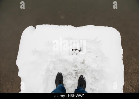 Piedi in mens stivali neri e i jeans sono in neve sul ponte prima di acqua Foto Stock