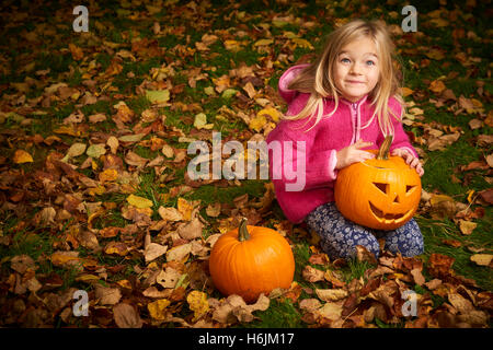 Bambino carina ragazza bionda giocando in foglie di autunno con zucca di Halloween. Foto Stock