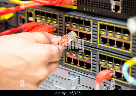 Mano collegando il cavo di fibra nell'interruttore nel data center Foto Stock