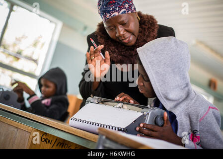 Un insegnante Ester Washinana aiuta i non vedenti allievo di utilizzare una macchina da scrivere braille durante la lezione di inglese a Eluwa scuola speciale in Ongwediva, Namibia Foto Stock